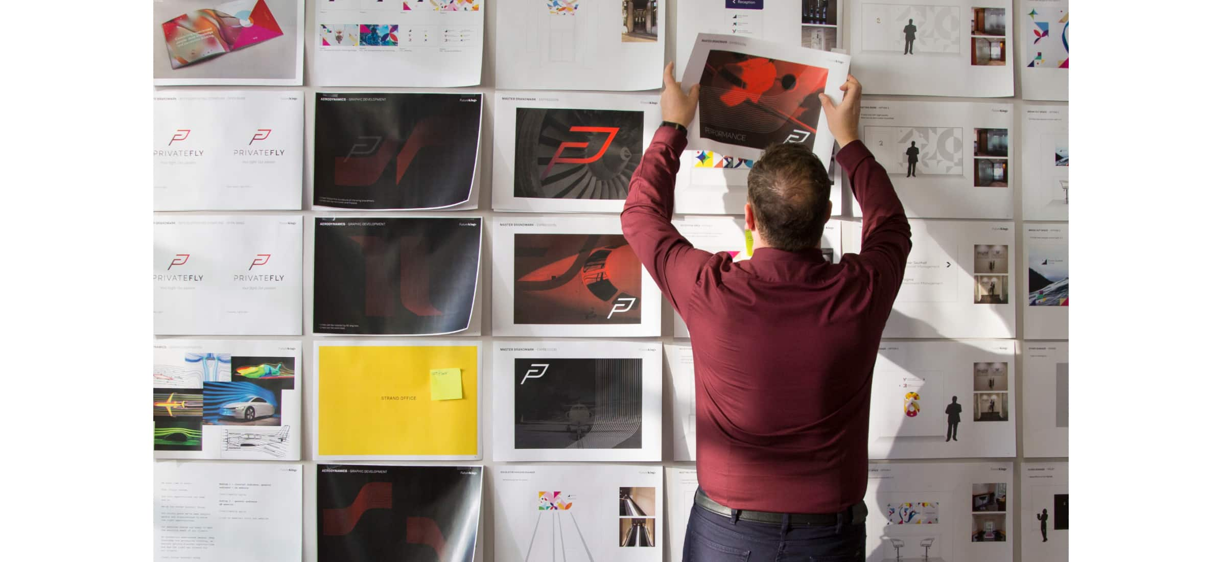 Steven reaching up to add an image on a piece of paper to a collection of other images attached to a wall.